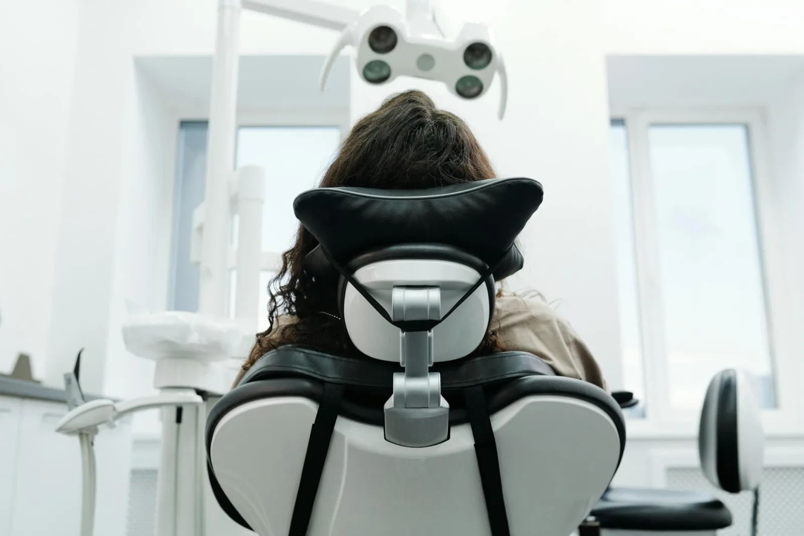 Someone reclined in a dental chair beneath the overhead light, seen from behind