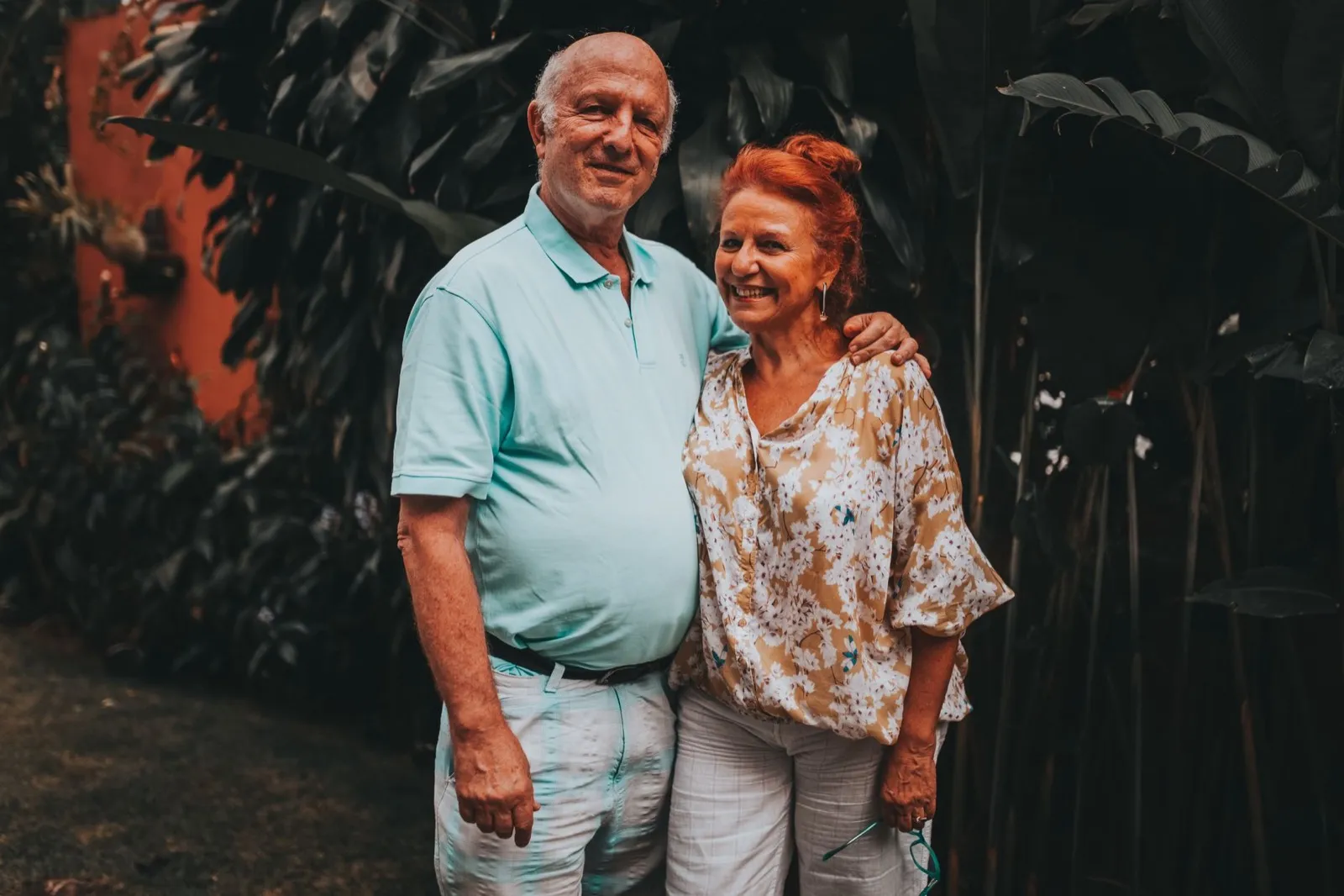 A couple in their sixties standing together outdoors, smiling.