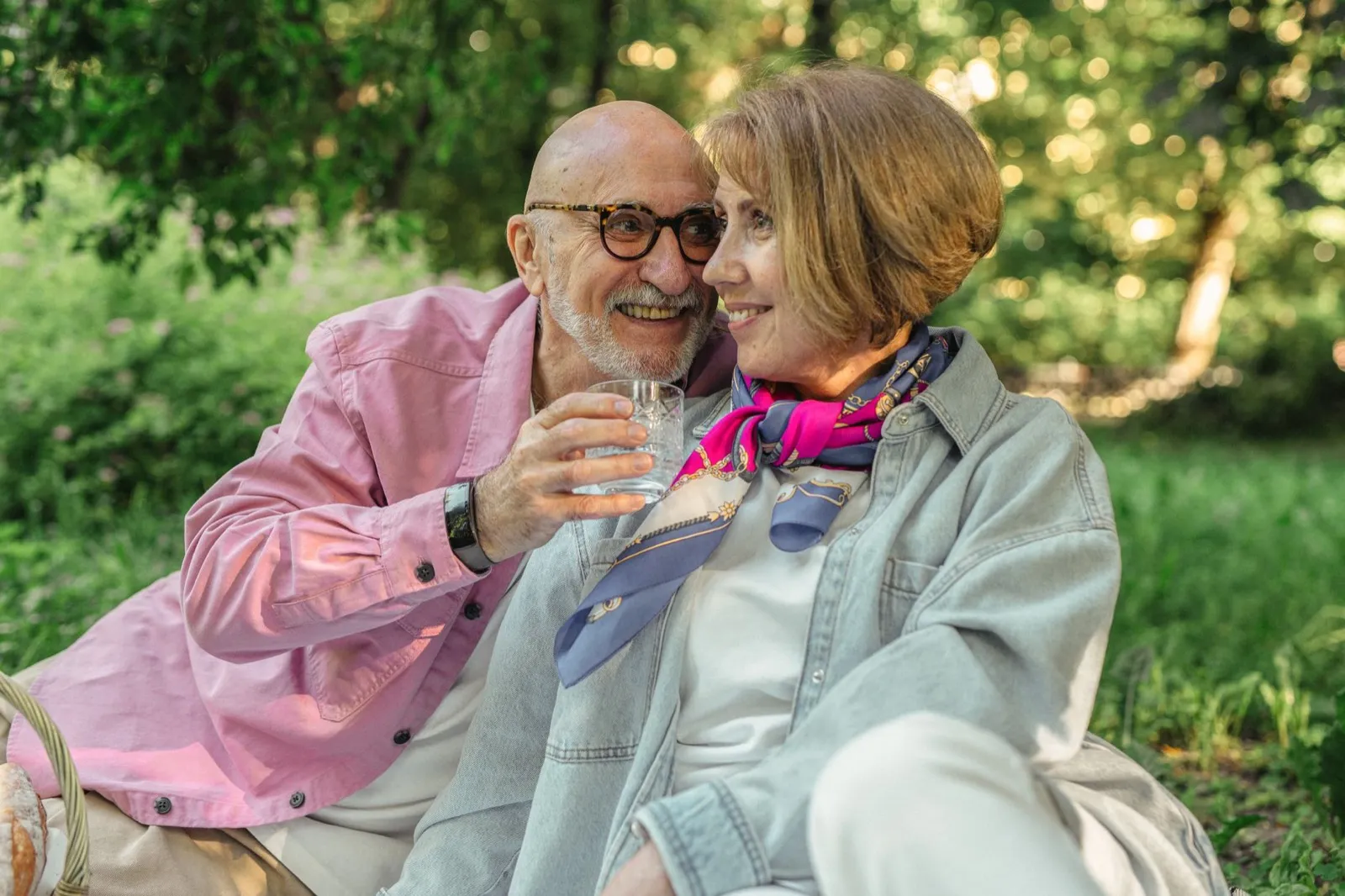 An older couple sitting outdoors in a park, relaxed and smiling.