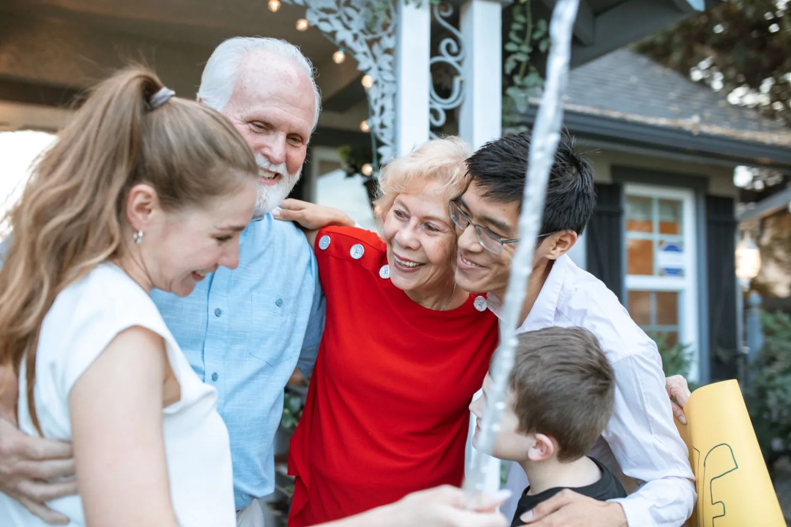 Three generations of a family embracing and laughing together outdoors.