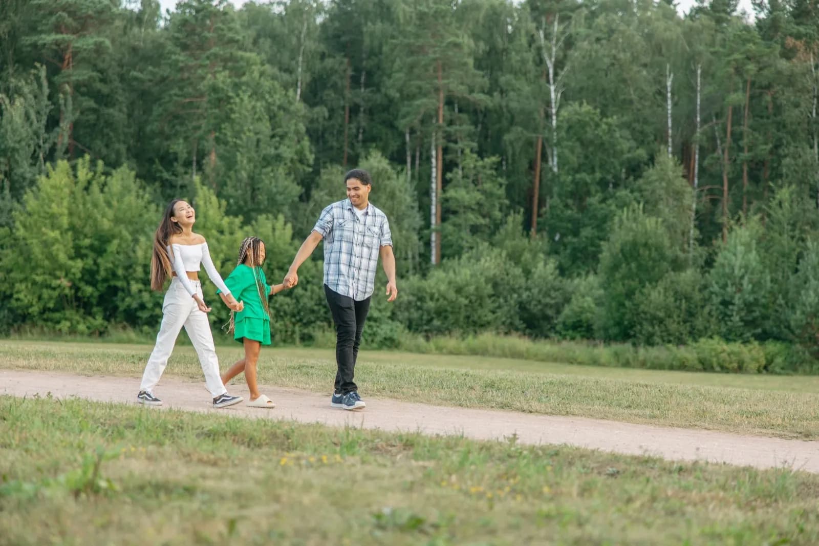 Two parents and a child walking hand in hand on a path beside woodland.