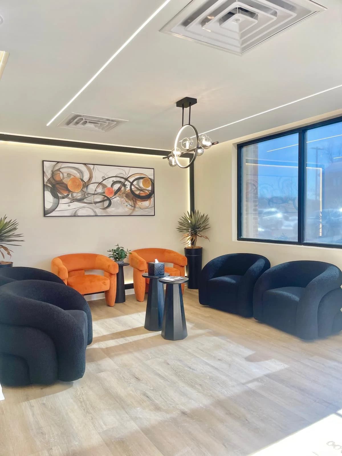 The waiting area at Advanced Dental Care of Stafford, with orange and navy armchairs, side tables and a large window